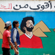 Egyptian youths walk in front of a picture of Liverpool's Egyptian forward Mohamed Salah with background of Great Pyramids, in Cairo, Egypt May 2, 2018. Arabic words read "You are stronger than drugs".